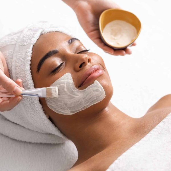 Top view of beauty therapist applying face mask on african woman skin, closeup